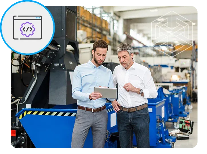 Two men in a factory setting, one holding a tablet looking at it, the other observing. In the background, manufacturing equipment and a stylized geometric cube illustration. A circular icon with code brackets and a gear is in the upper left.