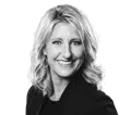 Black and white studio portrait of Becky Kelderman, Director of Sales, smiling and looking at the camera. She has blonde wavy hair and wears a dark blazer.