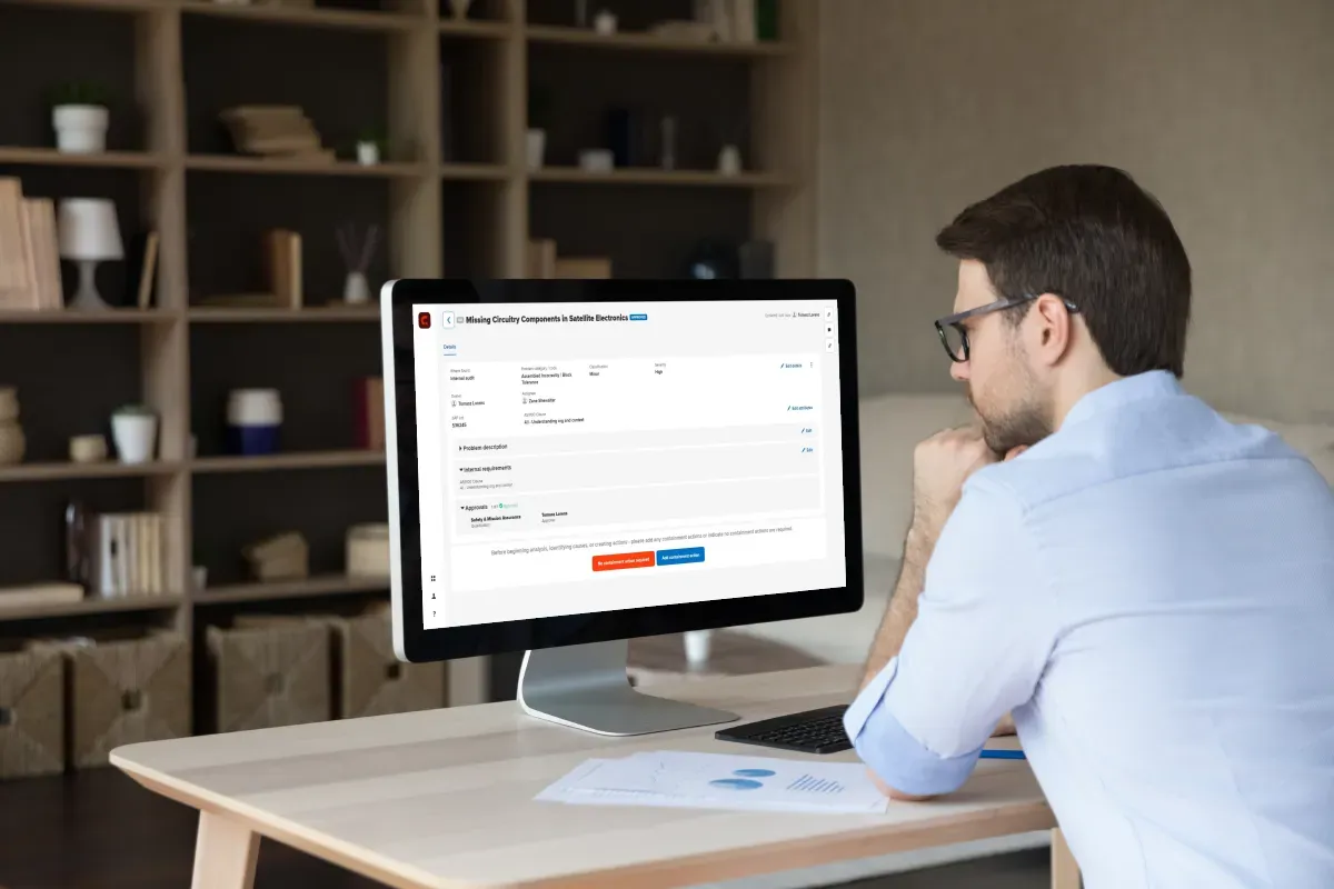 A man in glasses reviews a digital report titled Missing Circuitry Components in Satellite Electronics on a computer screen. The interface includes fields for details, problem description, and approvals, showcasing Manufacturo's quality management features.
