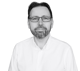 Black and white headshot of Tadeusz Dyduch, CEO of Manufacturo. He is wearing glasses and a white collared shirt and has a beard.